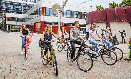 Studierende treffen sich mit ihren Fahrrädern vor dem Erweiterungsbau und Schloss